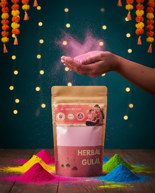 Hand holding pink gulal powder above a package of Amanvida Herbal Gulal with colorful gulal on a wooden surface.